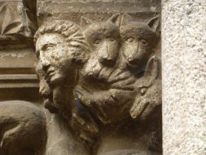 Figuras de lobos y una persona rezando, en un capitel de la portada de la iglesia de Santiago.